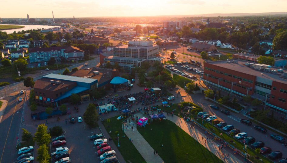 Wide aerial view of the Moncton skyline at dusk, overlooking the river, marshland and downtown buildings under a pastel evening sky.